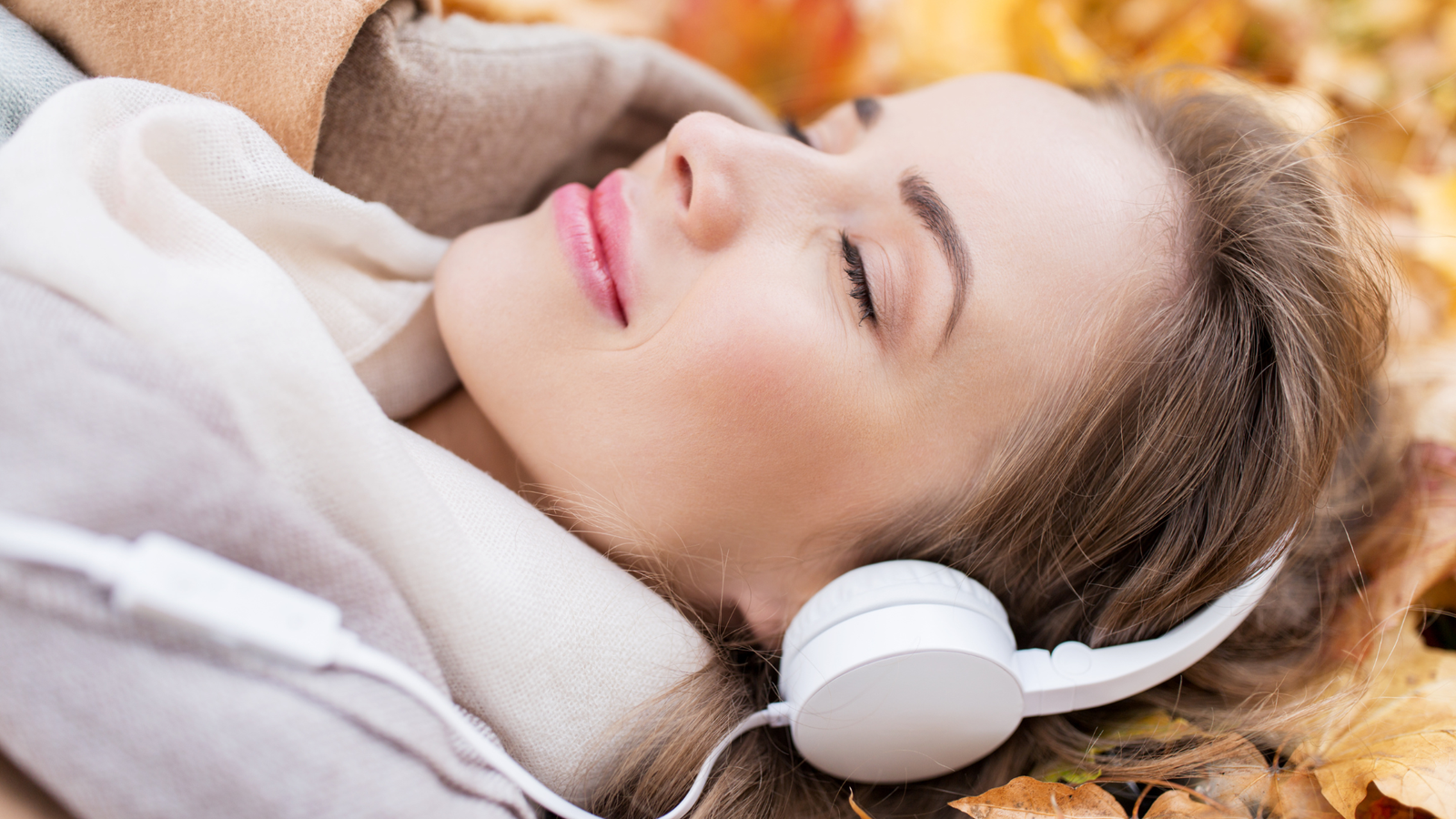 Woman lying on grass at sunrise with headphones, practicing a 5-minute neuro-sound focus routine.