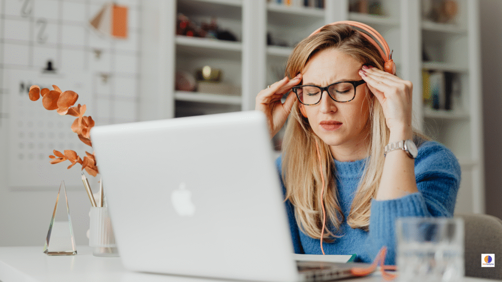 Woman working on a MacBook, looking tired and digitally fatigued after a long day online.