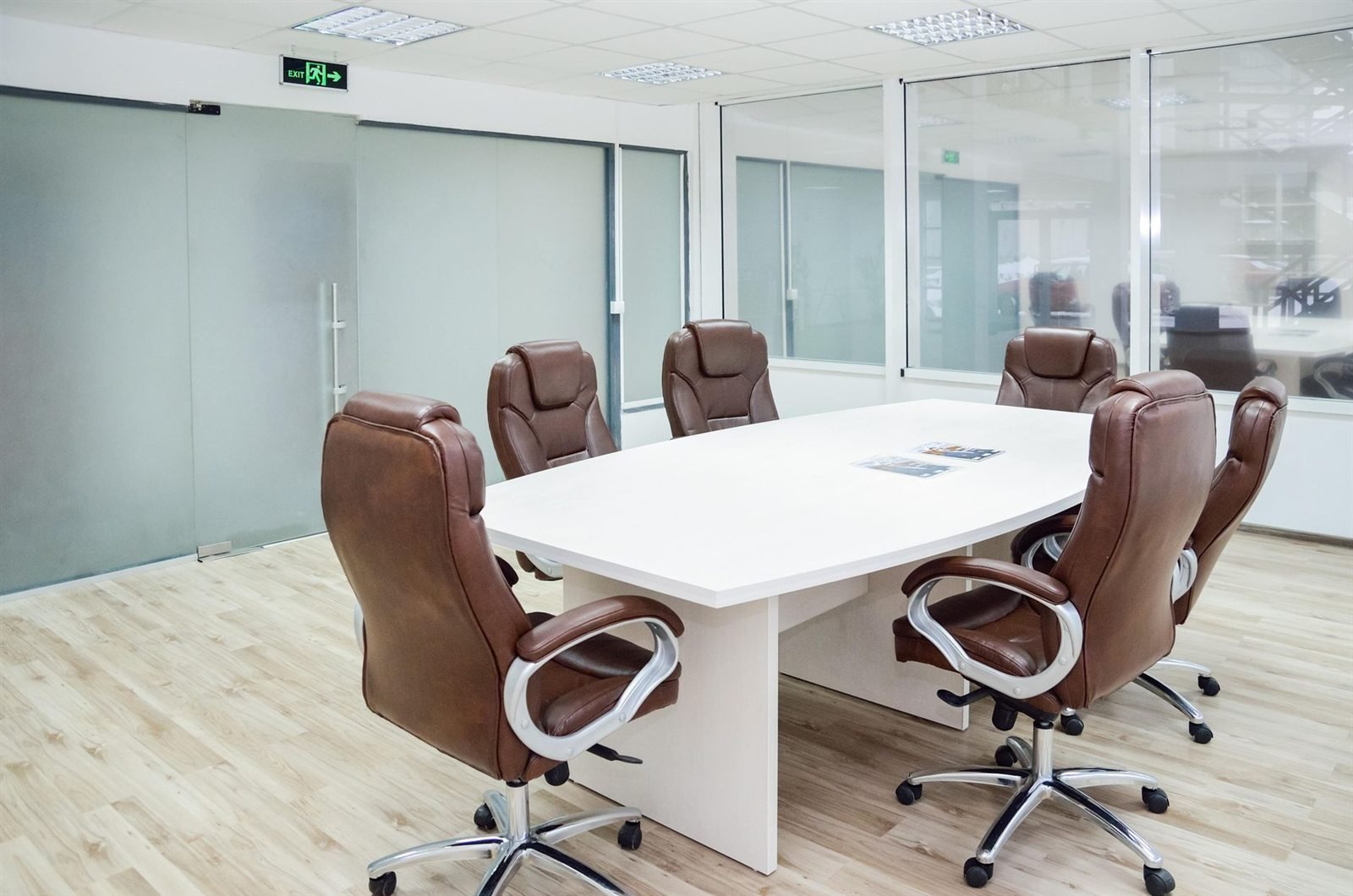 An empty glass-walled meeting room with a long table and chairs
